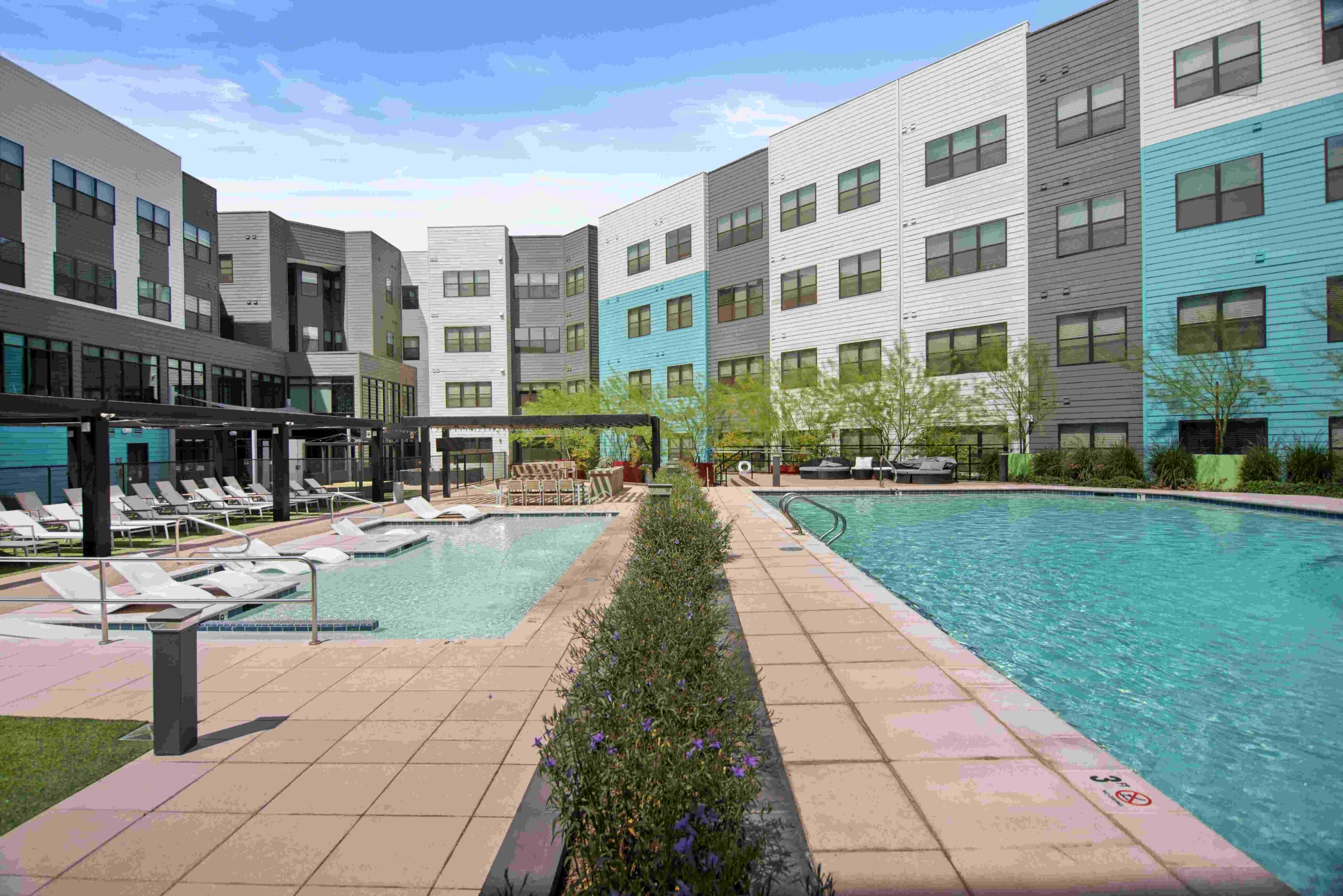 Apartment complex pool area with lounge chairs and surrounding greenery scaled