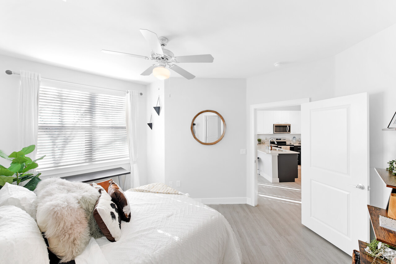 Bright bedroom with a bed mirror and open door to kitchen